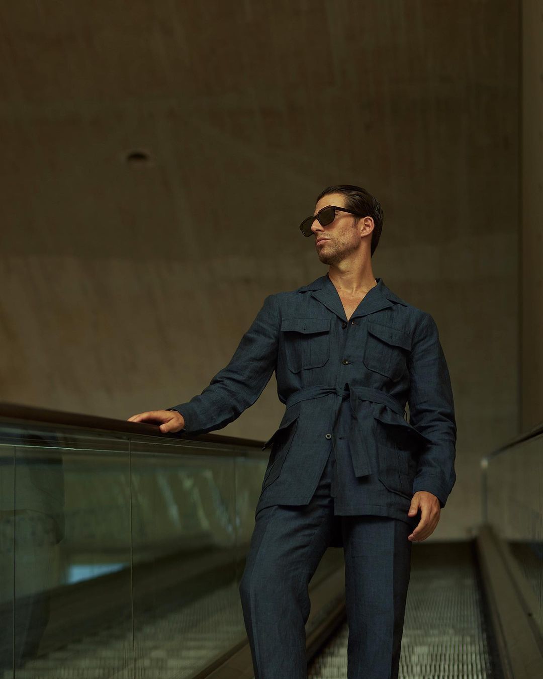 Model wearing the safari jacket in linen for men by Luxire in dark indigo on escalator